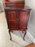 Closed view of the wooden jewelry chest with classic cabriole legs and polished finish, showing front doors closed.