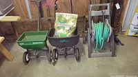 Lot of lawn care items: Scotts Speedy Green spreader, Ground Work spreader holding a Scotts EZ Seed bag, and beige hose reel with green hose