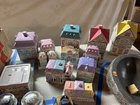 Twelve house-shaped porcelain canisters arranged on table, various pastel roof colors visible