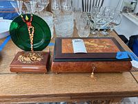 Two wooden music boxes and a green art glass plate on stand on a wooden table among glassware.