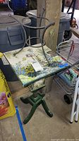 Hand-painted square table with two metal racks on top showing the painted floral and nature scene and green painted base.