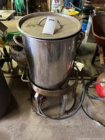 Full view of stainless steel large stick pot with lid on top of metal propane burner frame with hose attached on floor