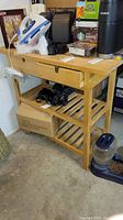 Frontal view of wooden rolling kitchen cart with drawers and items on top (not included)