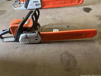 Full view of chainsaw with scabbard on guide bar, two saws visible