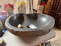 Stone sink basin with rough outer edges, smooth dark grey hollow inside, central drain hole, and visible scratches. Tag inside reads 'two buttons'.