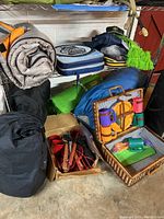 Overview of camping gear on shelving: tent, sleeping bags, stadium cushions, and picnic basket with cups and plates.