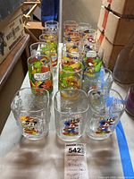 Overhead view of 14 vintage collectible glasses featuring Mickey, Minnie, Muppets, and Peanuts characters with colorful designs.