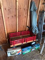 Red Berlin Flyer wagon with black wheels, wooden slats, branding, next to boxed Bocce set and Golf QuikNet net, indoor wood-paneled background
