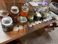 Wide view showing 10 Yankee Candle jars of different scents and sizes, a row of white ceramic tea light candles in holder forming a line in front.
