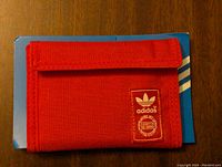 Front view of the red Adidas nylon wallet showing the Velcro flap closure and Adidas logo patch.