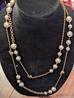 Front view of the gold-colored chain necklace with alternating large and small faux silver pearls draped on black display, showing length and pearl arrangement.