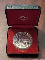 1980 Canadian Dollar coin displayed inside a red velvet-lined box with a maple leaf emblem on the lid. Coin housed in a clear capsule.