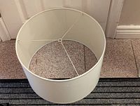 White cylindrical lampshade viewed from above, showing internal metal support structure and fabric condition.
