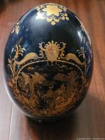 Front view of black ceramic Satsuma egg with gold dragon and bird decoration.