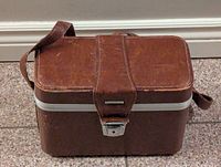 Front view of vintage brown leather binocular case showing metal latch and central leather strap.