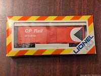 Front of original box showing red Canadian Pacific Rail boxcar model T-20105 through clear window. Box has yellow and red diagonal stripes around window and Lionel HO logo in corner.