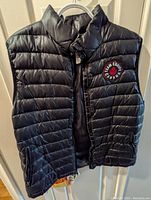Front view of black puffer vest showing Team Canada patch on left chest, zipper closure, and puffer horizontal quilting.