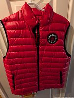 Front view of men's red puffer vest showing zipper, Team Canada black circular patch, and side pockets with zippers.
