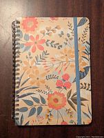 Front cover of the floral notebook with elastic band and black spiral binding visible on the left.