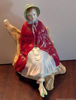 Front view of Royal Doulton Sally HN 2741 figurine displaying detailed hand-painted woman seated on a rustic bench with a red cape and green bonnet.