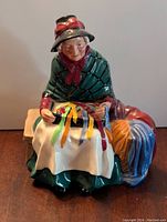 Front view of the Royal Doulton Silks and Ribbons HN2017 porcelain figurine showing the elderly woman seated with colorful ribbons on a white cloth, box yarn beside her on the bench.