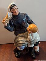 Front view of Royal Doulton figurine showing sailor with white cap holding a seashell and a child with a sailboat toy.