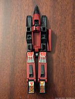 Top view of Transformers G1 Thrust figure showing front side with red and black coloring and silver and yellow stickers. Missing some parts, one panel detached and set aside.