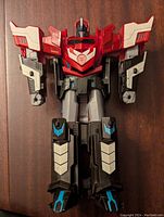 Front view of Optimus Prime figure in robot mode showing detailed sculpt and paint with red torso and black legs, blue and white accents.