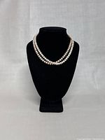 Two vintage pearl necklaces displayed on a black bust, showing length and design.