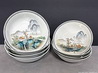 Two stacks of bowls: left stack of four large, right stack of four medium, showing matching landscape scenes.