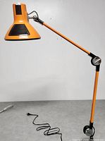 Close-up of orange lamp head, black vent accents, adjustable arm segment and chrome pivot joint
