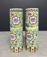 Pair of cylindrical porcelain vases showing front floral designs and colors