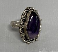 Close-up front view of vintage silver ring with amethyst cabochon gemstone and ornate silver bezel setting.