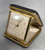 Front view of the open BIRKS travel alarm clock showing the clock face and gold-tone frame, with black leather case partially visible.