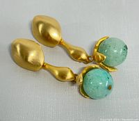 Front side view showing teardrop-shaped green jade held in gold tone metal prongs with textured gold tone clip-on backing visible from rear markings.