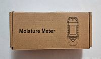 Brown cardboard box labeled 'Moisture Meter' with simple graphic of device on top.