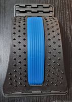 Black orthopedic back stretcher with blue ribbed support pad, covered with small massage nodes and adjustable multi-level base.