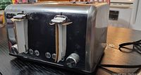 Side view of CUSIMAX stainless steel 4-slice bread toaster with two lever handles and front buttons and dial for functions.
