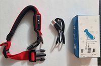 Red USB rechargeable LED dog collar with USB charging port, black plastic buckle, USB cable and original box packaging shown on white surface.