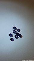 Nine natural royal blue round cabochon sapphires arranged on a white surface, showing smooth domed shapes and deep blue coloration.