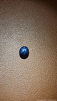 Photo of oval blue star sapphire cabochon showing the 6-ray star effect on textured brown surface.