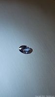 Oval natural blue sapphire gemstone shown alone on a flat surface with light showing facets and color