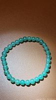 Photo of the green Aventurine bracelet laid flat on a brown surface, showing the entire circle of polished round beads.