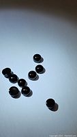 10 small round jet black onyx cabochon gemstones arranged on a white surface, reflecting light and showing glossy finish.