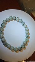 Kiwi jasper beaded bracelet laid flat on a white circular surface, showing the round natural beads with pale green and black inclusions.