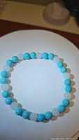 Photo of a stretchy bracelet with alternating white jade and light blue turquoise beads placed on a white display stand.