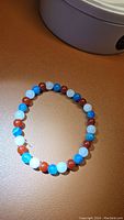 Photo showing bracelet laid flat with visible beads of white, blue and red colors polished on elastic string.