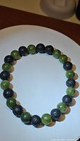 Full view of the stretchy beaded bracelet composed of green jade and black porous lava stone beads, displayed on a white plate background.