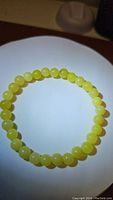 Photo showing a circular bracelet made of smooth, round, polished lemon jade beads in a light yellow-green color under direct light.