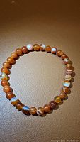 Photo of the red agate bead stretchy bracelet laid flat on a tan surface showing round banded beads with natural patterns.